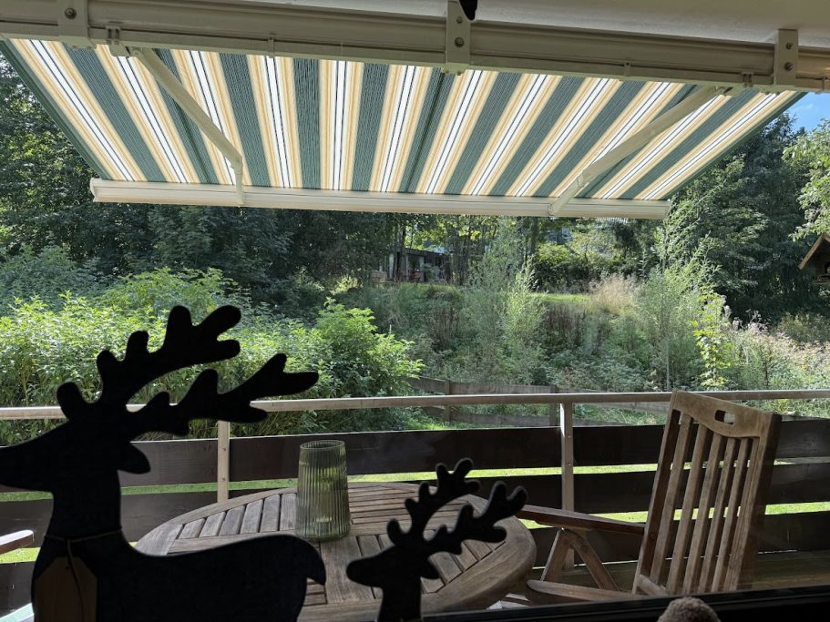 2 Balkone mit Blick ins Grüne Blick auf eine grüne Landschaft durch ein gestreiftes Markise, mit einem Holzstuhl im Vordergrund.